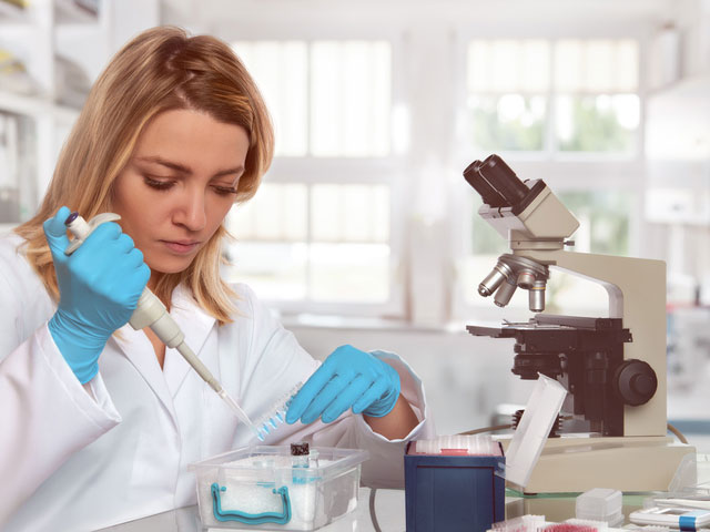 Жена у белом мантилу ради у лабораторији поред микроскопа
